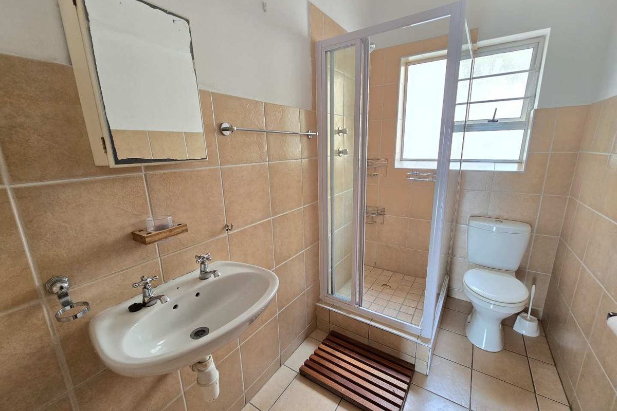 A functional bathroom featuring a pedestal basin, a shower enclosure, and a toilet, finished with neutral wall and floor tiling.