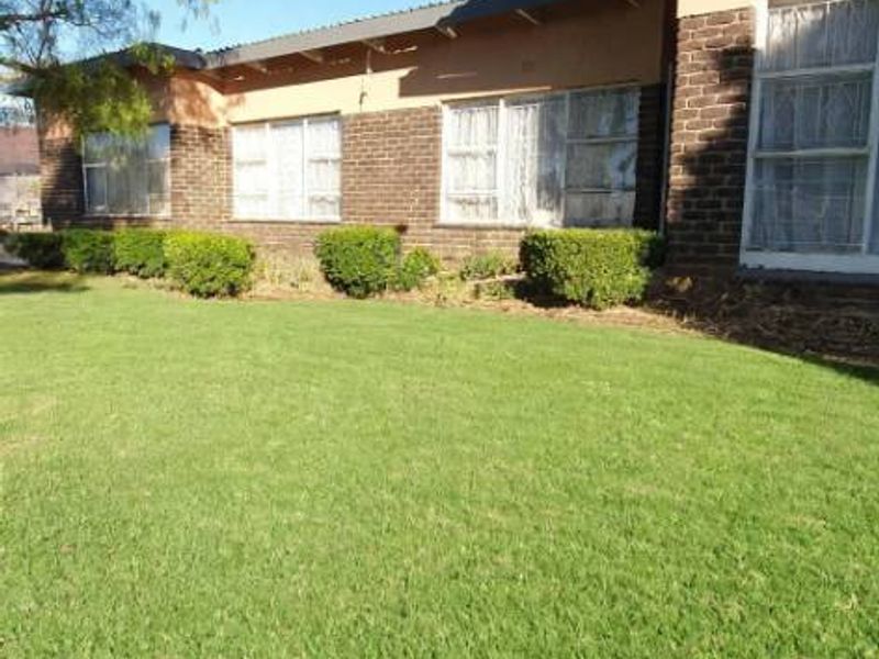 Rear view of the house featuring a brick facade, aluminum window frames, and a well-maintained lawn with established garden hedges.