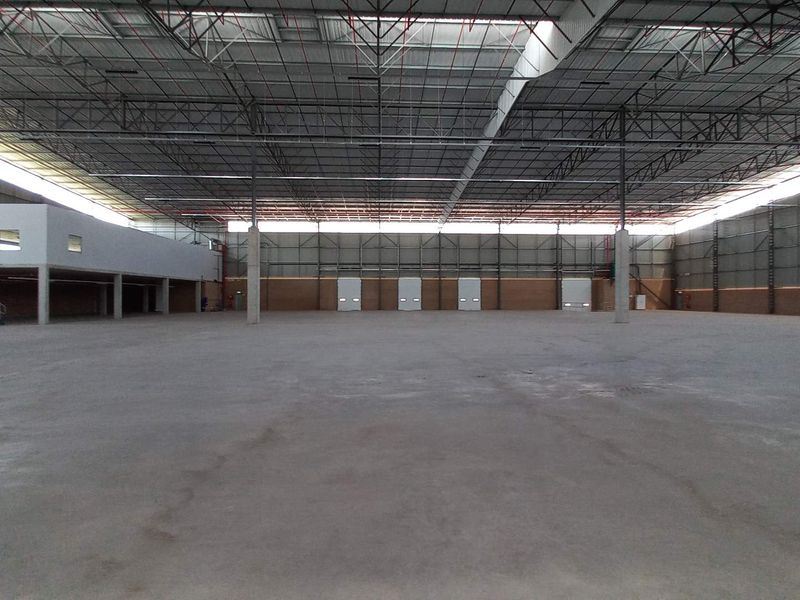 Expansive industrial warehouse space featuring high ceilings with exposed steel trusses, concrete flooring, a mezzanine level, and multiple loading bay doors.