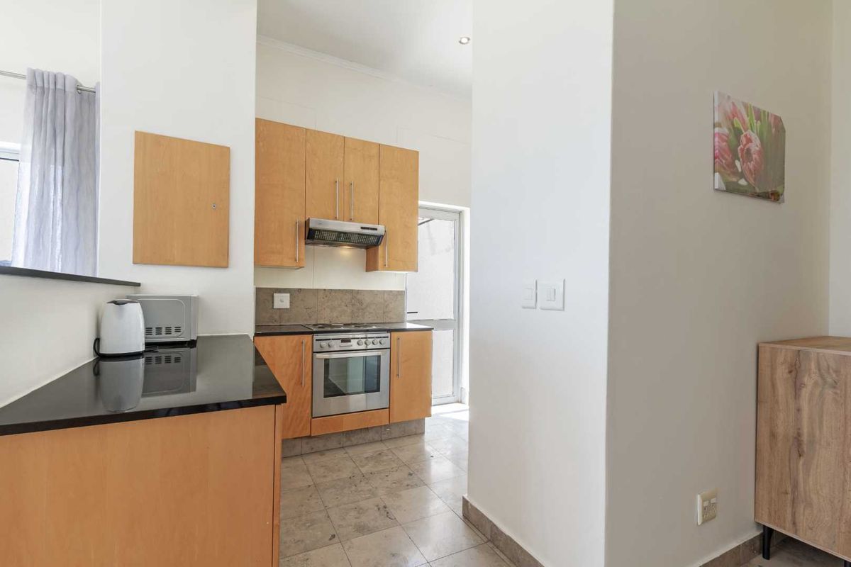 A functional kitchen featuring light wood cabinetry, black countertops, a built-in oven with extractor fan, and tiled flooring with direct access to the exterior.