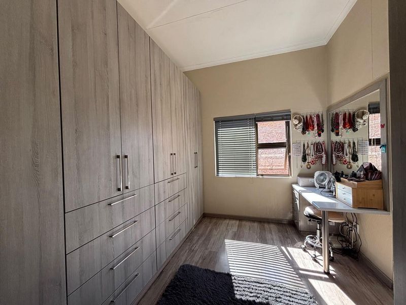 A well-maintained bedroom featuring extensive floor-to-ceiling built-in cupboards, modern laminate flooring, and natural light through a window with venetian blinds.