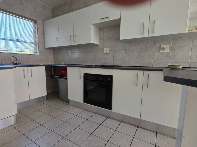 Functional kitchen featuring white cabinetry, dark laminate countertops, tiled backsplash, and built-in oven with hob, offering a practical layout for daily use.