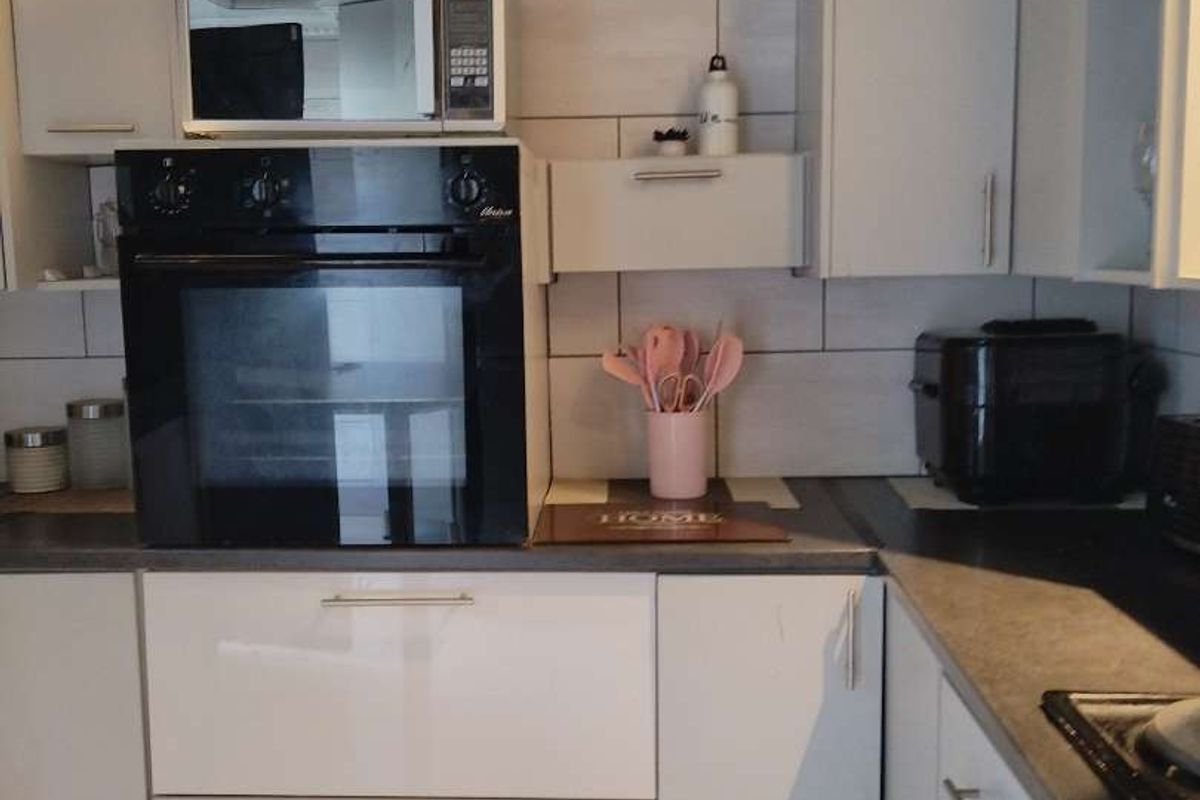 A modern kitchen featuring white cabinetry, dark laminate countertops, a tiled backsplash, and integrated appliances including a built-in oven and microwave.