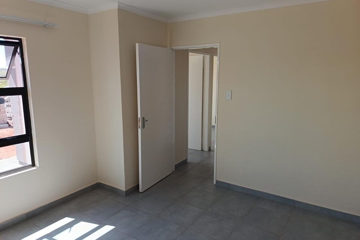 A bright, empty bedroom featuring neutral wall paint, grey floor tiles, and a modern white interior door.