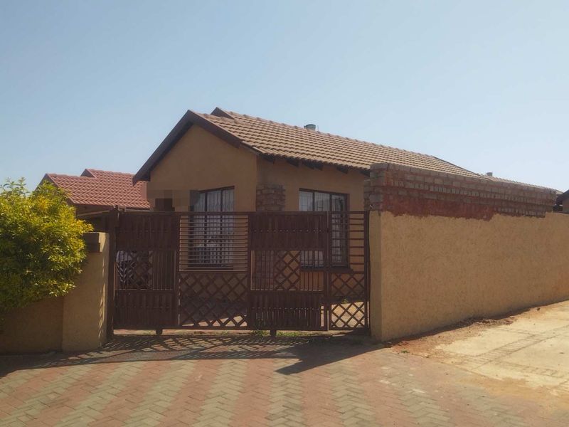 Front view of a single-story house featuring a tiled roof, secure metal gate, and a paved driveway with a perimeter wall.