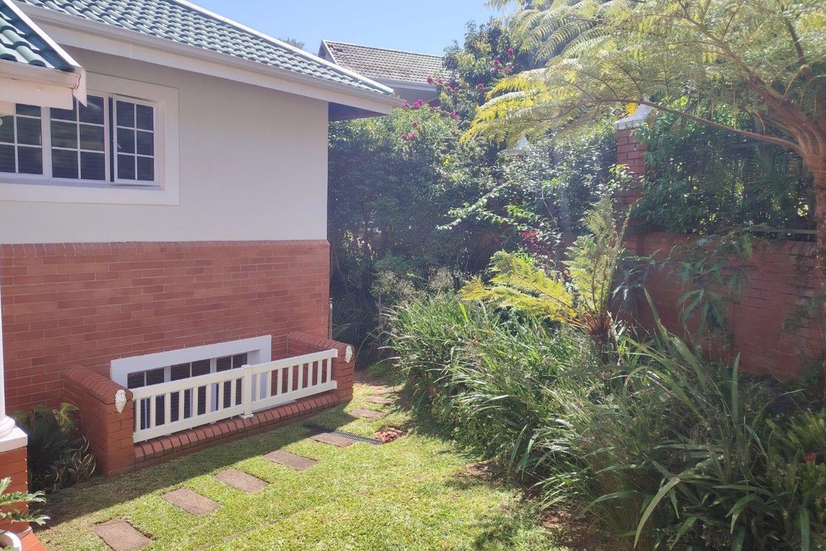 A well-maintained rear garden area featuring a brick facade, tiled roof, and established landscaping with a brick boundary wall.