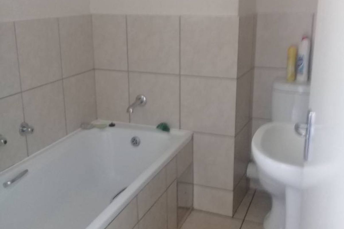 A functional bathroom featuring a bathtub, pedestal basin, and toilet with neutral wall and floor tiling.