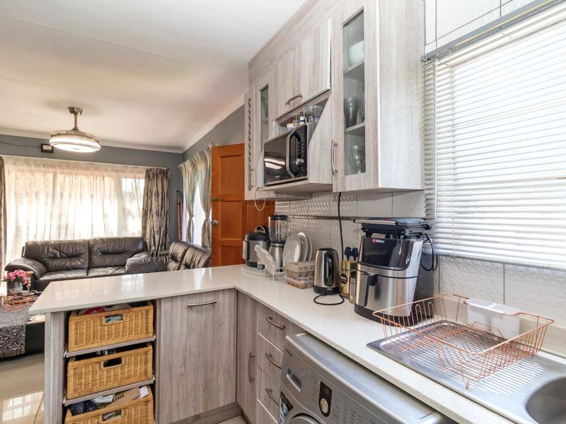 Open-plan kitchen and living area featuring modern light-wood cabinetry, stone countertops, and integrated laundry facilities, flowing into a comfortable lounge space.