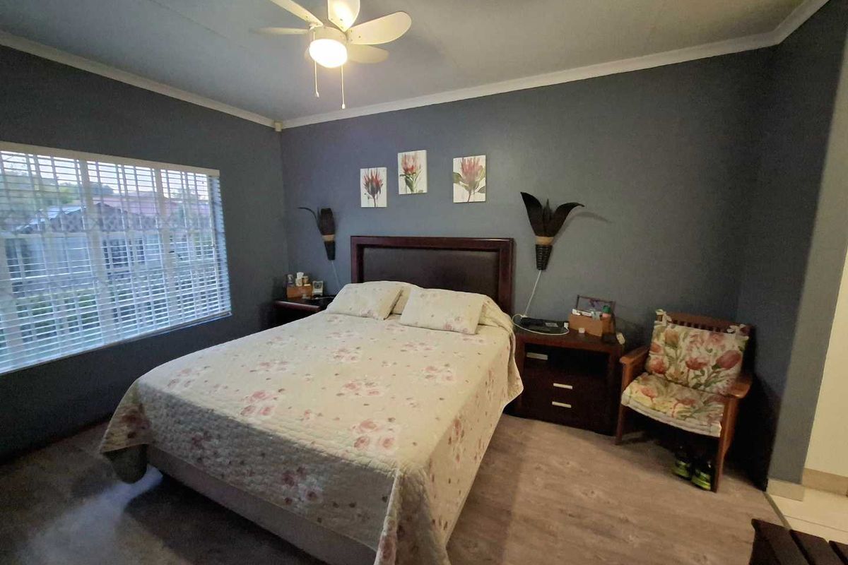 A well-lit bedroom featuring laminate flooring, a ceiling fan, and window blinds, providing a comfortable and functional living space.