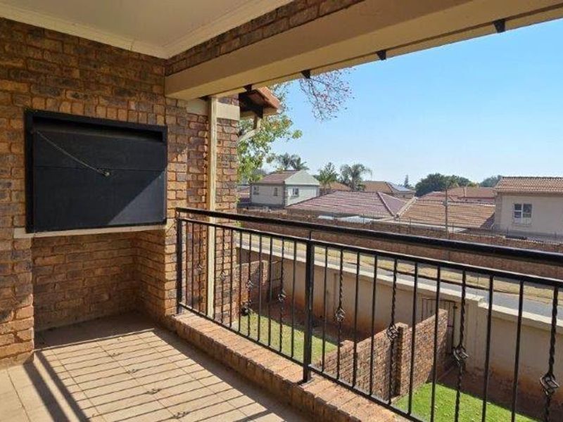A covered balcony featuring a built-in braai, brick wall finishes, and metal railings, offering an elevated view of the surrounding residential area.
