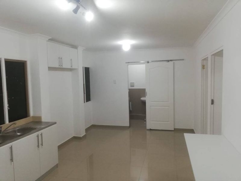 An open-plan living and kitchen area featuring tiled flooring, white cabinetry, and a sliding door leading to an adjacent room.