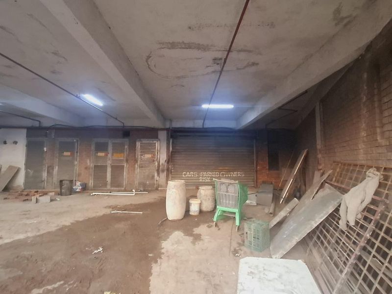 Spacious industrial garage area featuring exposed concrete ceilings, roller shutter doors, and brick wall finishes, suitable for storage or parking.