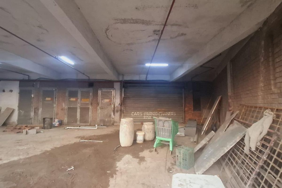 Spacious industrial garage area featuring exposed concrete ceilings, roller shutter doors, and brick wall finishes, suitable for storage or parking.