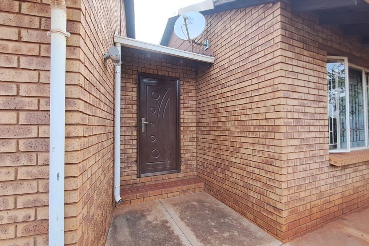 A side entrance featuring a brown security door, brick facade, and a satellite dish mounted on the exterior wall.