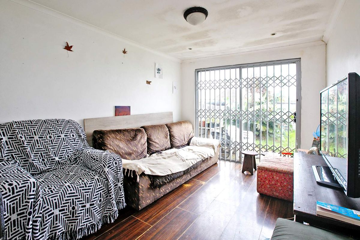 A living room featuring dark wood-look flooring, a sliding glass door with security gate, and ceiling light fixture.