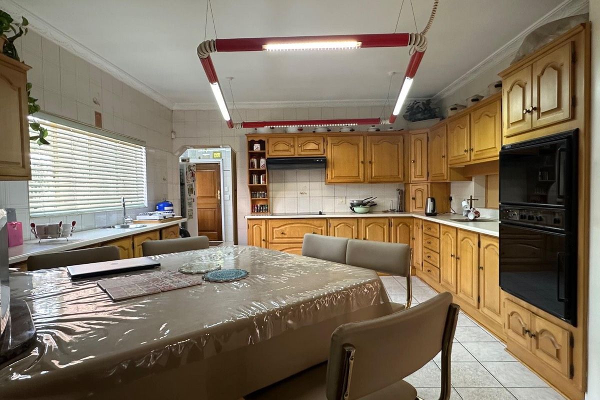 Spacious kitchen featuring traditional timber cabinetry, integrated double oven, tiled splashbacks, and a central dining area with tiled flooring.