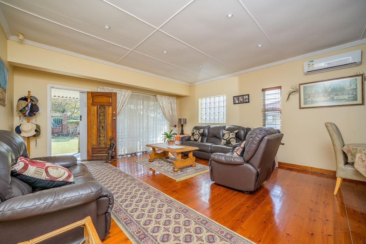Spacious living room featuring polished hardwood flooring, recessed lighting, a split-system air conditioner, and a glass block window with direct access to the garden.