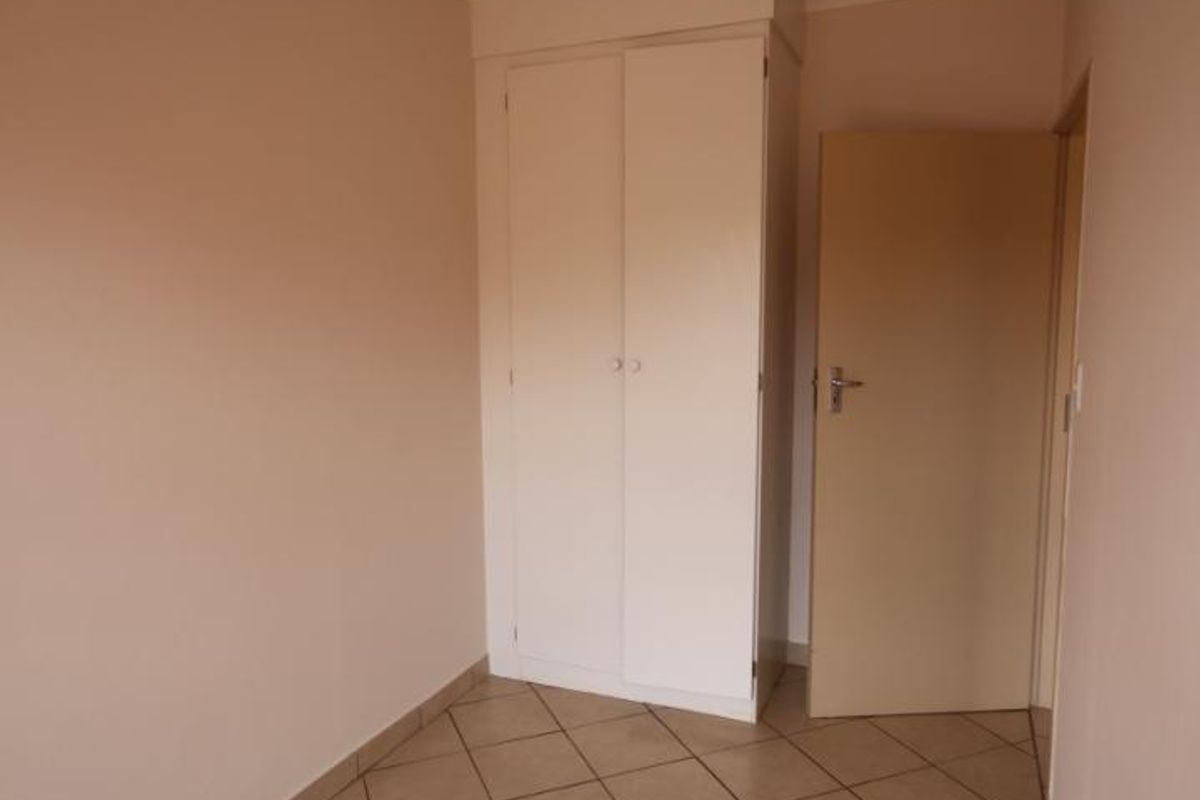 A compact, empty bedroom featuring neutral wall paint, tiled flooring, and a built-in wardrobe.