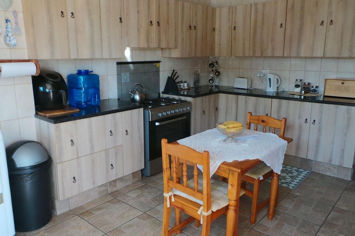 Functional kitchen featuring light wood-look laminate cabinetry, dark granite countertops, a freestanding gas stove, and tiled flooring throughout.