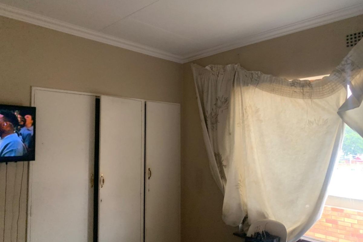 A bedroom featuring built-in cupboards and a window with natural light, requiring cosmetic updates to the wall finishes.