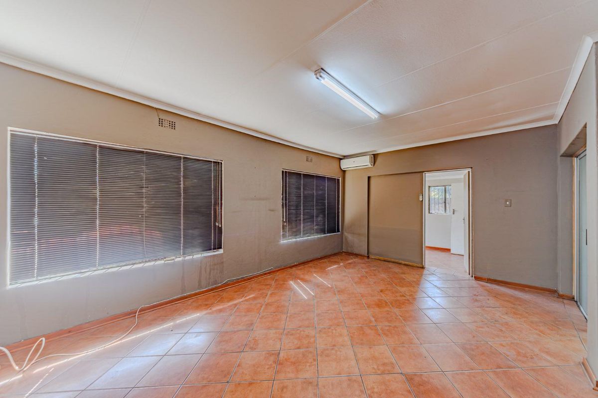 An empty living room featuring tiled flooring, an air conditioning unit, and venetian blinds, offering a neutral space ready for personalization.