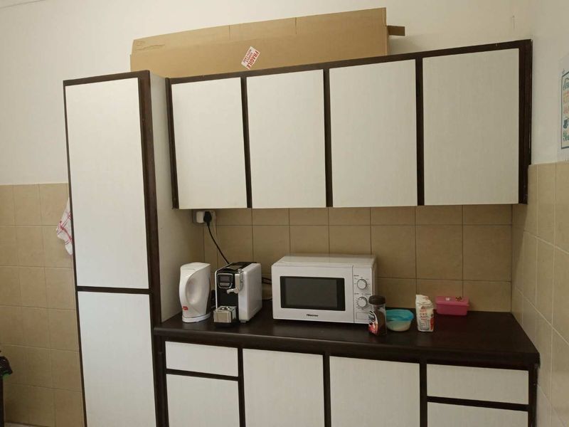 A functional office kitchenette featuring white cabinetry with dark trim, a dark laminate countertop, and a tiled backsplash.