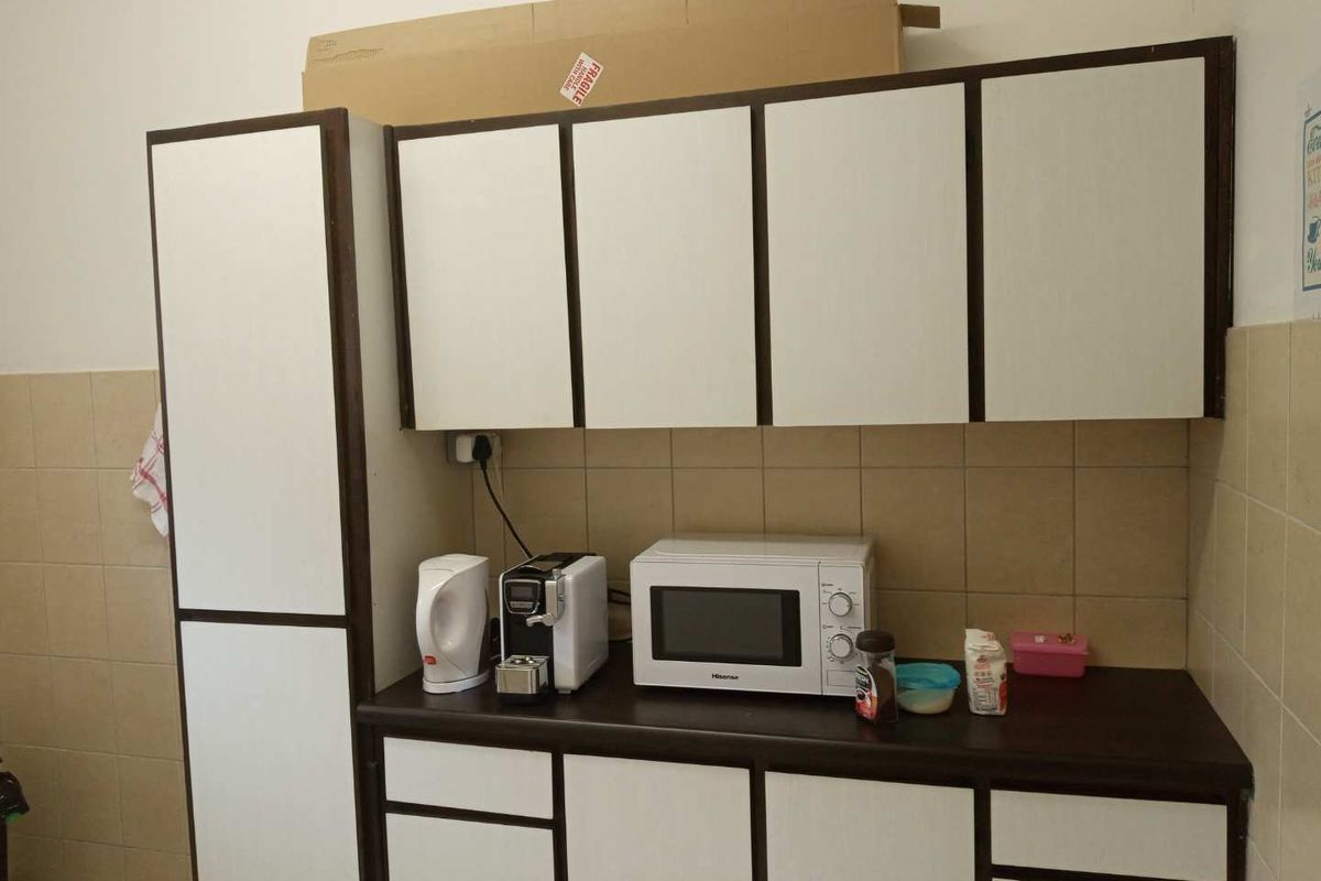 A functional office kitchenette featuring white cabinetry with dark trim, a dark laminate countertop, and a tiled backsplash.