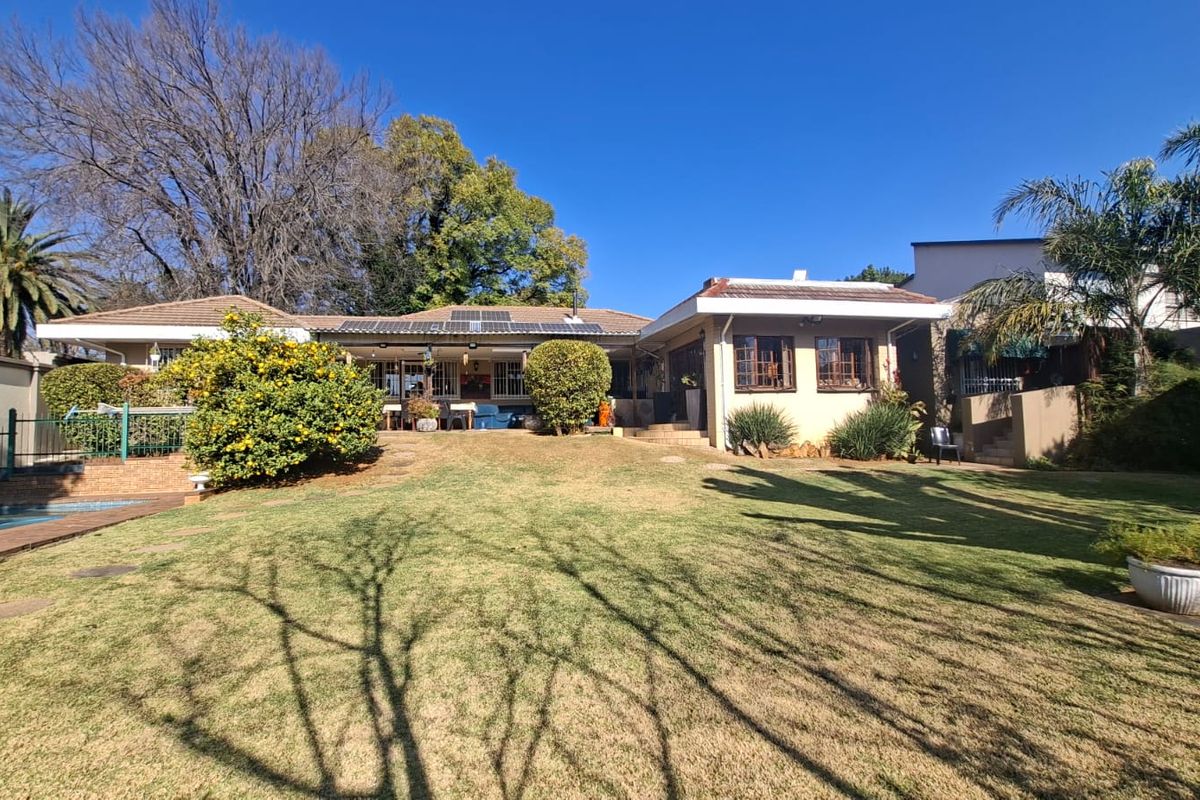 Rear view of the property featuring a spacious lawn, swimming pool, covered patio area, and roof-mounted solar panels.