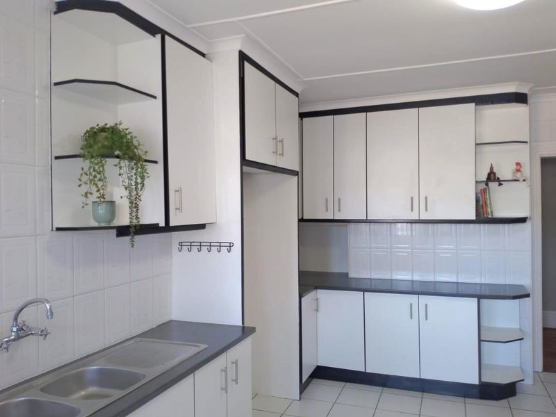 A clean, functional kitchen featuring white cabinetry with dark trim, tiled splashbacks, and a double bowl sink.