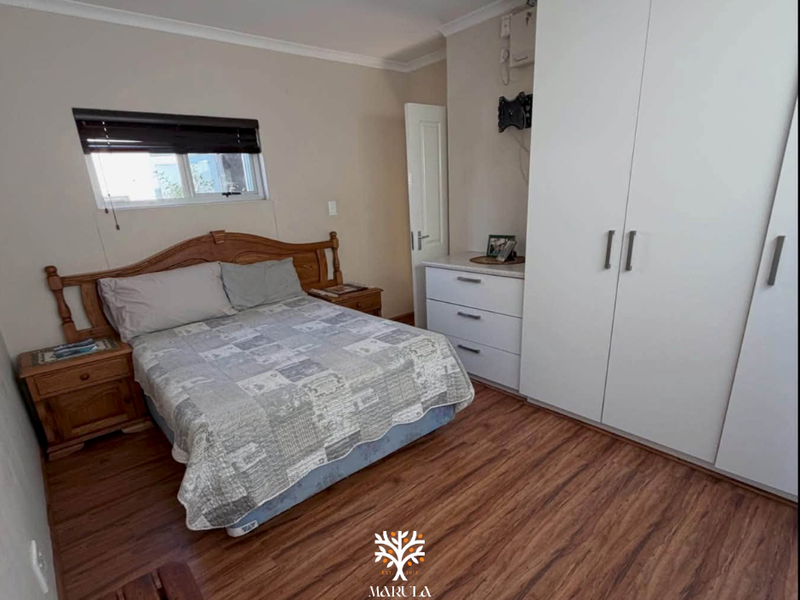A functional bedroom featuring laminate flooring, built-in cupboards, and a window with fitted blinds.