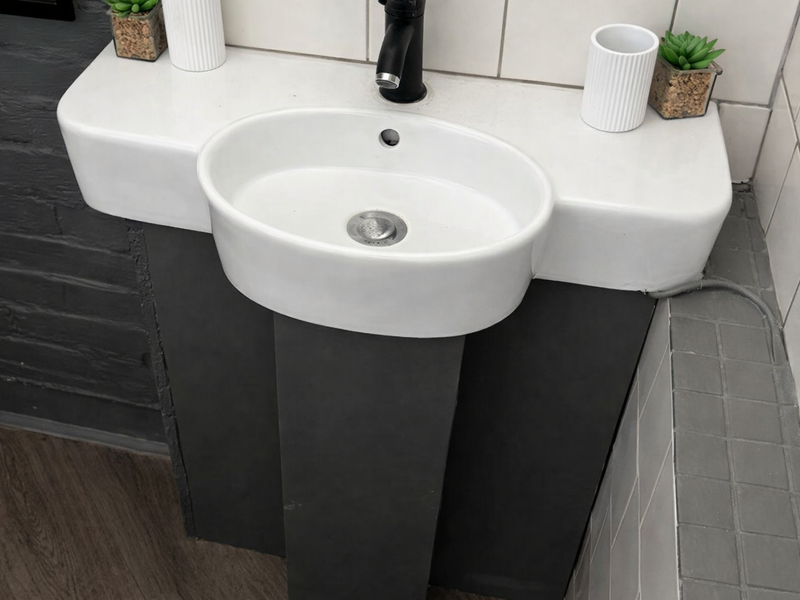 A modern bathroom vanity featuring a white pedestal basin with a sleek black mixer tap, complemented by subway wall tiles and mosaic floor tiling.