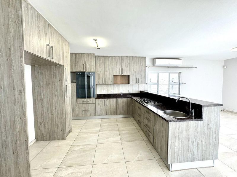 Modern open-plan kitchen featuring wood-grain cabinetry, dark granite countertops, integrated double oven, gas hob, and tiled flooring.