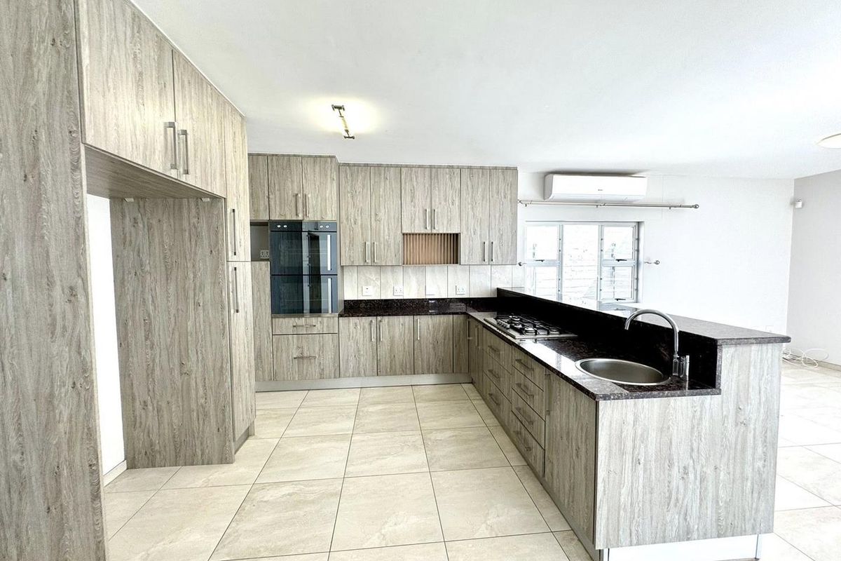Modern open-plan kitchen featuring wood-grain cabinetry, dark granite countertops, integrated double oven, gas hob, and tiled flooring.