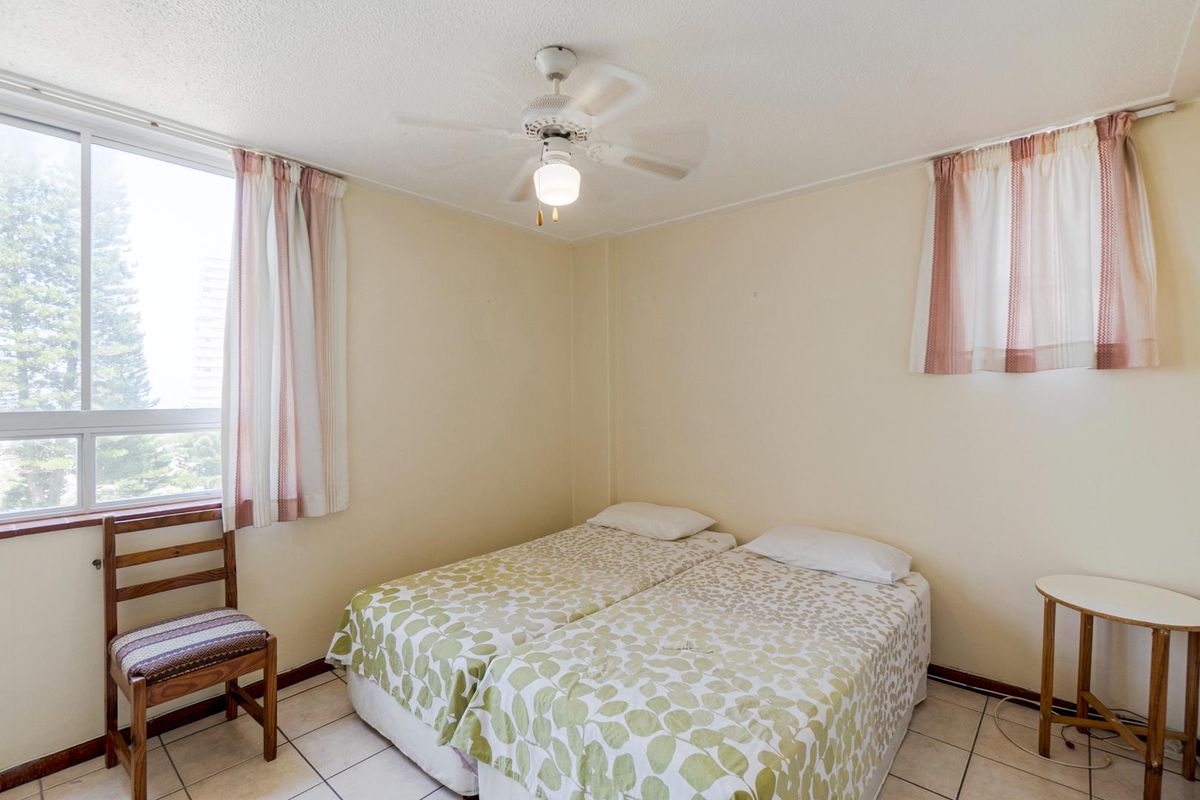 A functional bedroom featuring tiled flooring, a ceiling fan, and large windows that provide natural light.