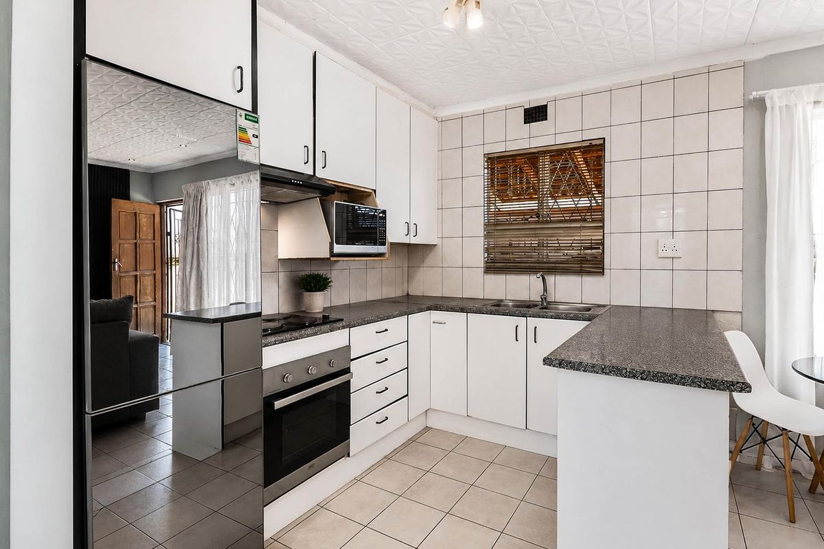 A functional kitchen featuring white cabinetry, granite-look countertops, a built-in oven, hob, and extractor fan, with tiled flooring and backsplash.
