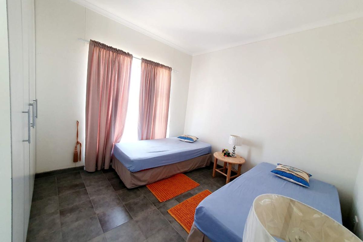A bedroom featuring tiled flooring, built-in cupboards, and large windows with curtains, providing a functional and well-lit living space.