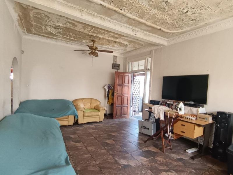 A living room featuring tiled flooring, a ceiling fan, and an ornate plaster ceiling that requires significant repair and restoration.