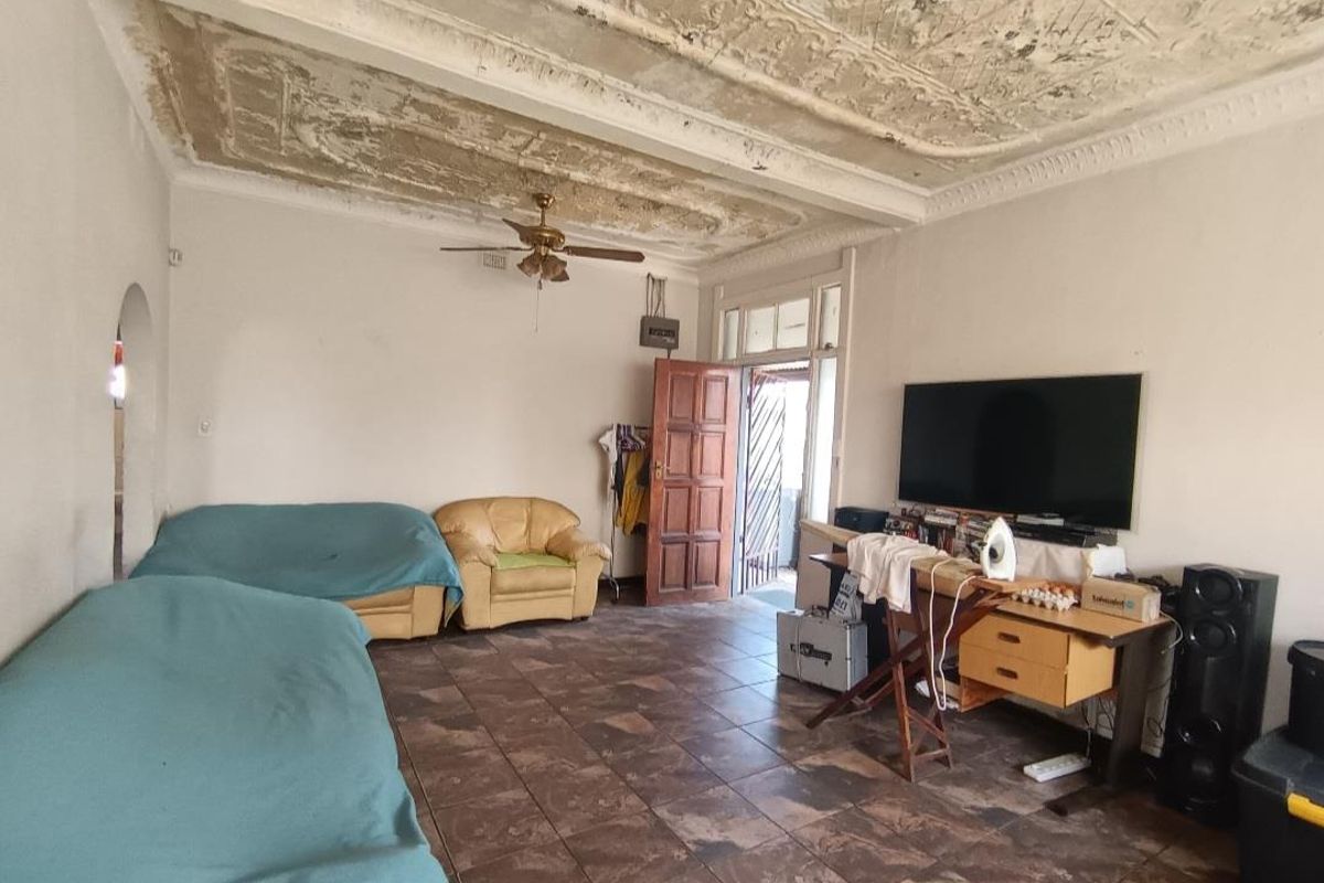 A living room featuring tiled flooring, a ceiling fan, and an ornate plaster ceiling that requires significant repair and restoration.