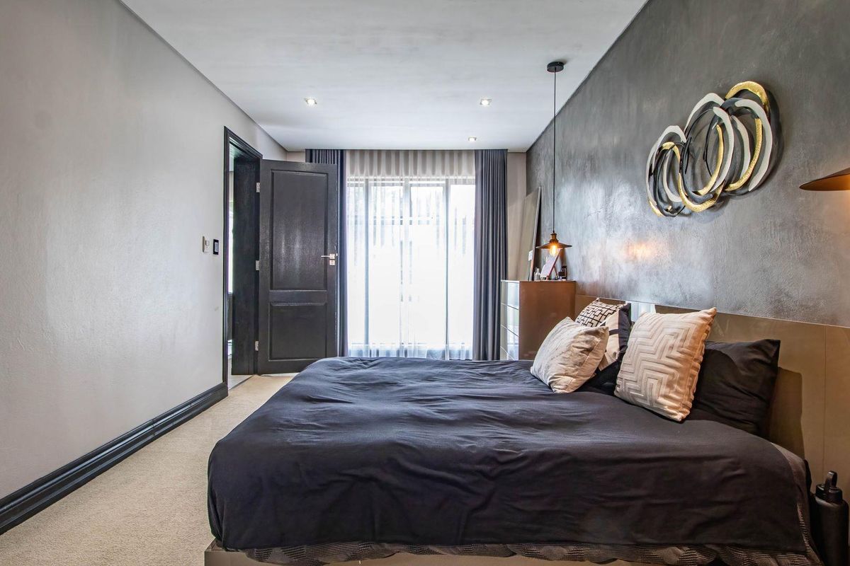 A modern bedroom featuring a textured feature wall, recessed ceiling lighting, and neutral carpeting.