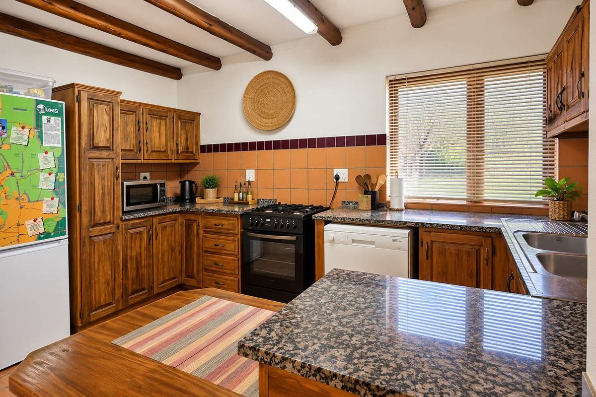 A functional kitchen featuring warm wooden cabinetry, granite countertops, a gas stove, and exposed wooden ceiling beams, providing a rustic and practical workspace.