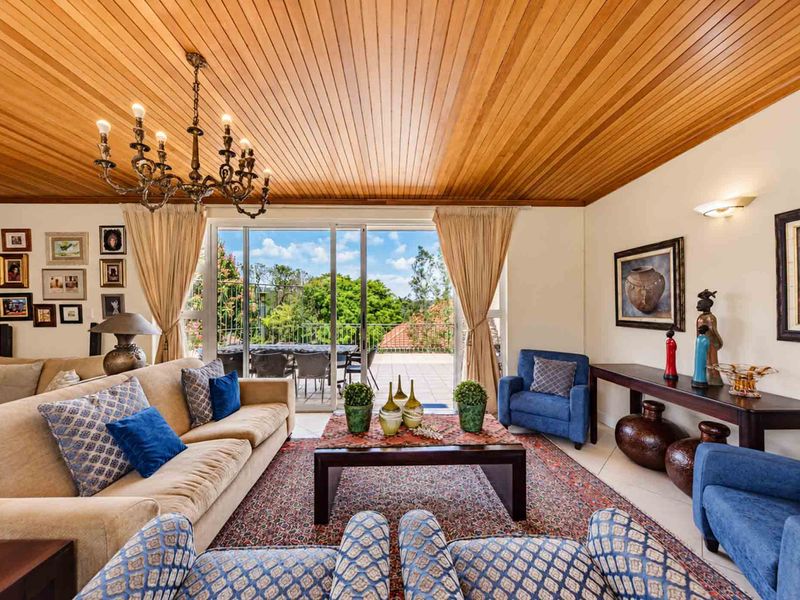 Spacious living room featuring a warm timber tongue and groove ceiling, classic chandelier, and large sliding glass doors opening to an outdoor patio area.