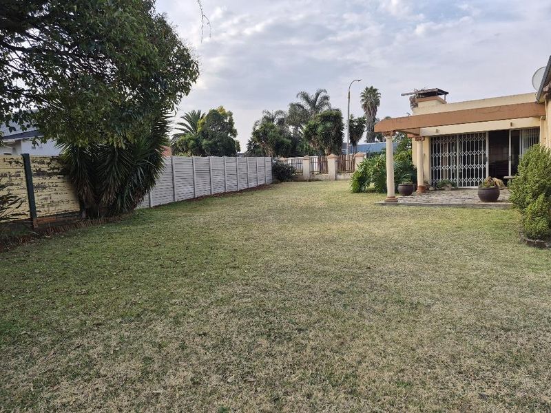 Spacious rear garden featuring a covered patio with concrete columns, paved flooring, and a perimeter precast concrete wall.