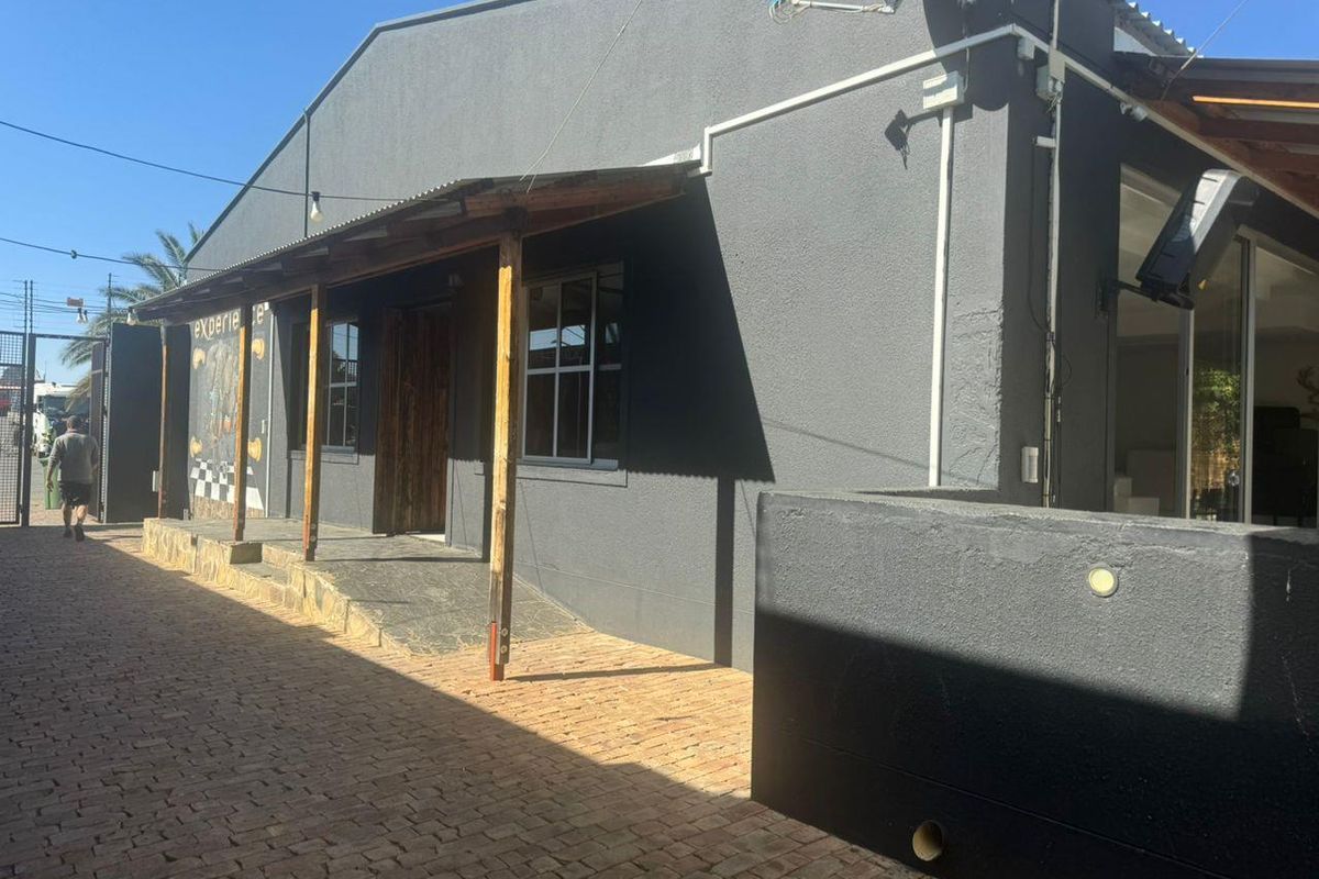Exterior view of an industrial property featuring a dark grey facade, covered walkway with timber supports, and brick paved access area.
