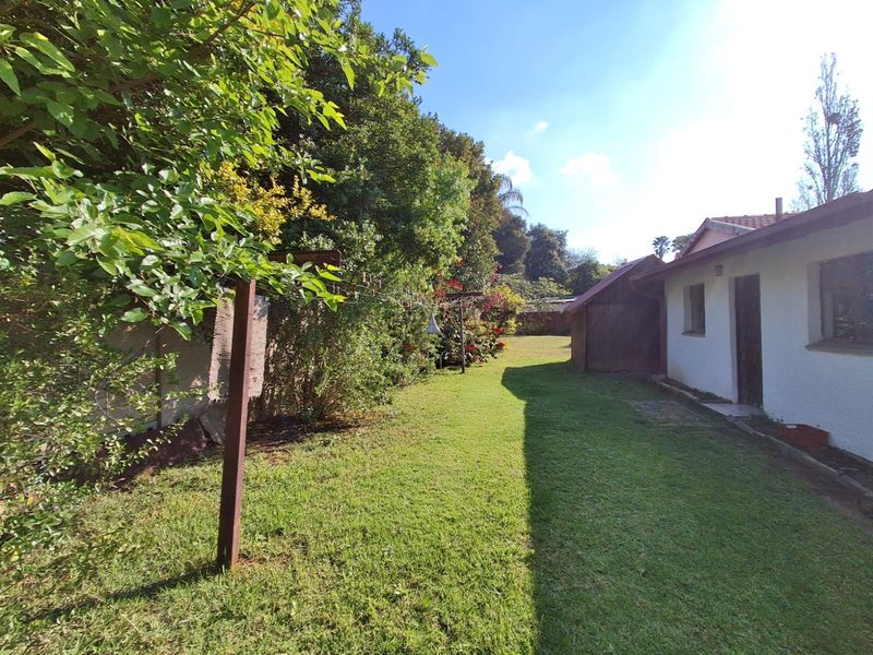 A view of the rear garden area featuring a well-maintained lawn, mature landscaping, and the side elevation of the house.