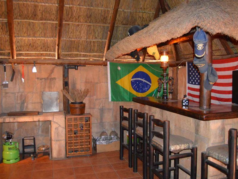 Outdoor entertainment area featuring a thatched roof, built-in stone braai, and a rustic bar counter with tiled flooring.