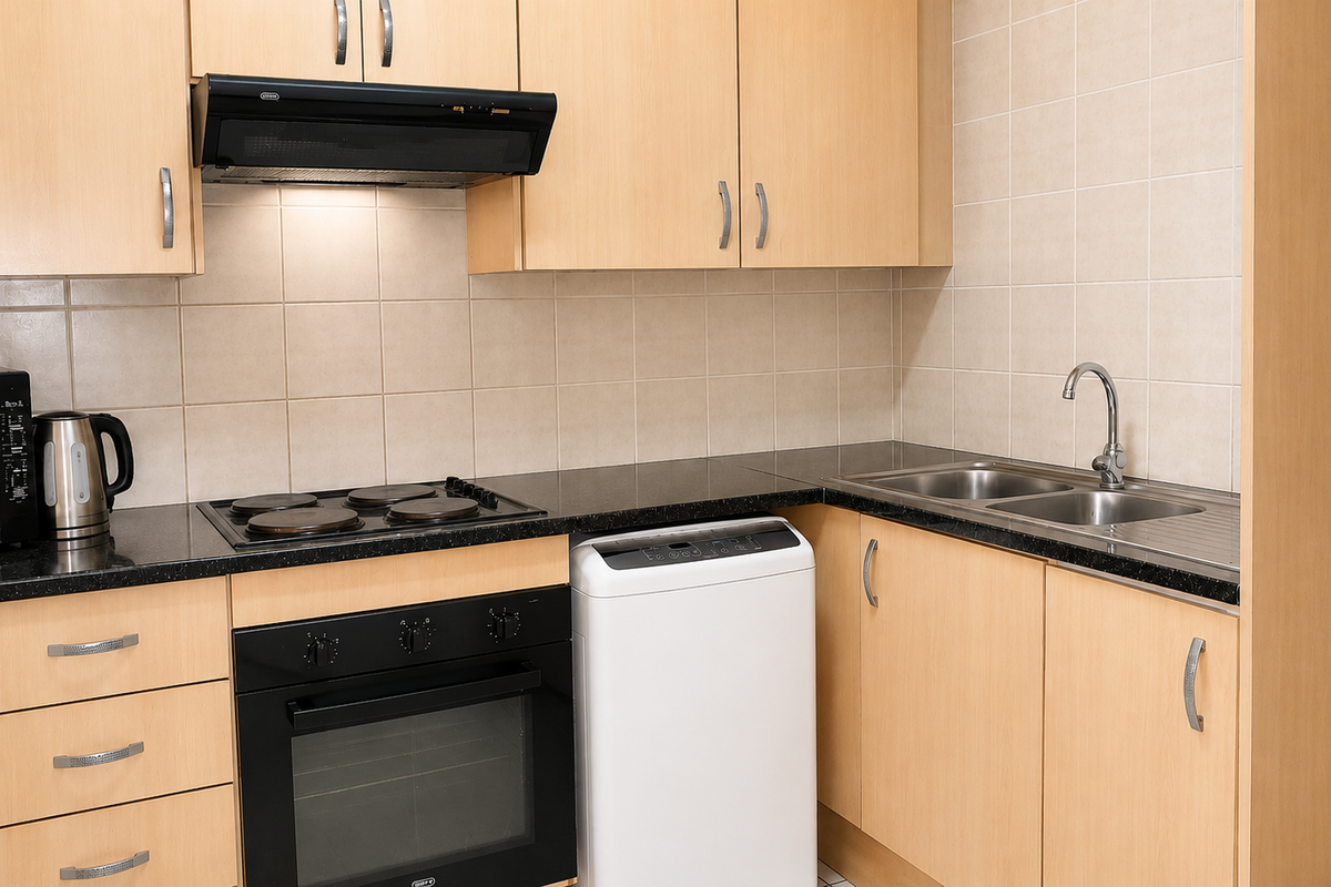 A functional kitchen featuring light wood-finish cabinetry, dark granite countertops, a built-in oven with electric hob, and a double stainless steel sink.