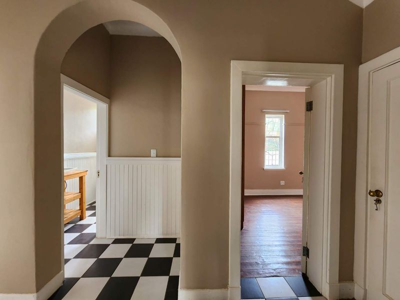 A bright hallway featuring a classic arched entryway, white wainscoting, and a striking black and white checkerboard floor leading into adjacent rooms.