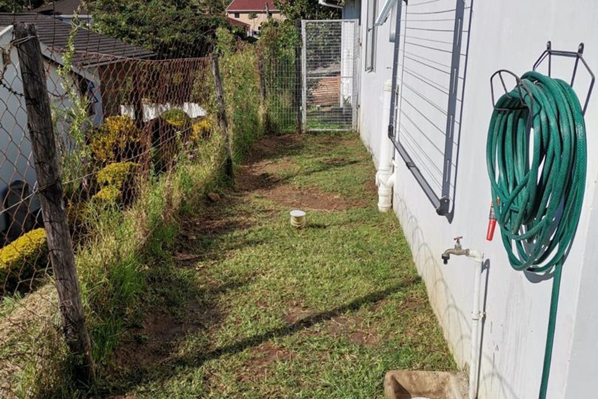 A narrow rear exterior side passage featuring a wall-mounted clothesline, external water tap, and drainage point, enclosed by chain-link fencing.