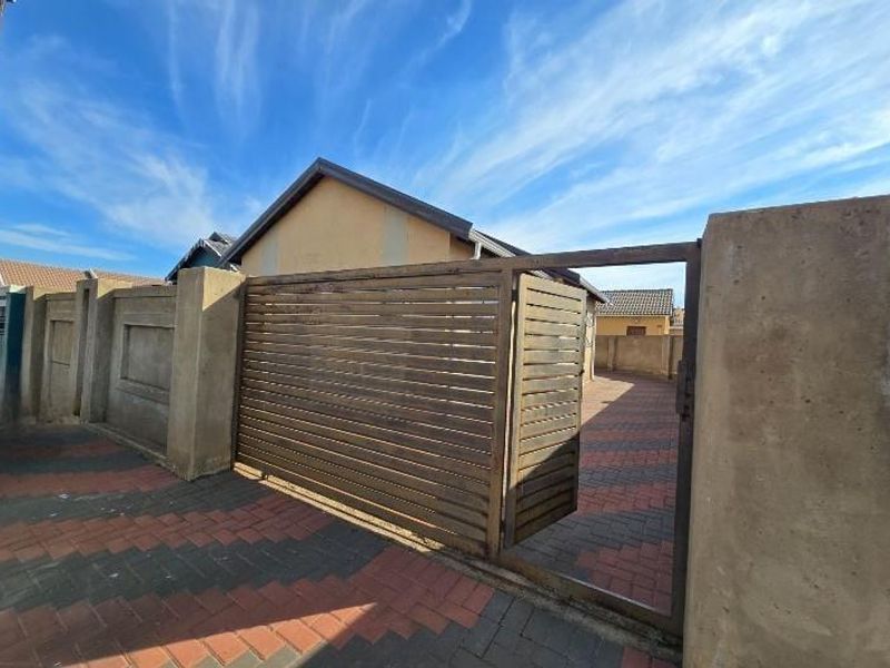 Front entrance view featuring a paved driveway, perimeter wall, and a slatted metal gate providing access to the property.