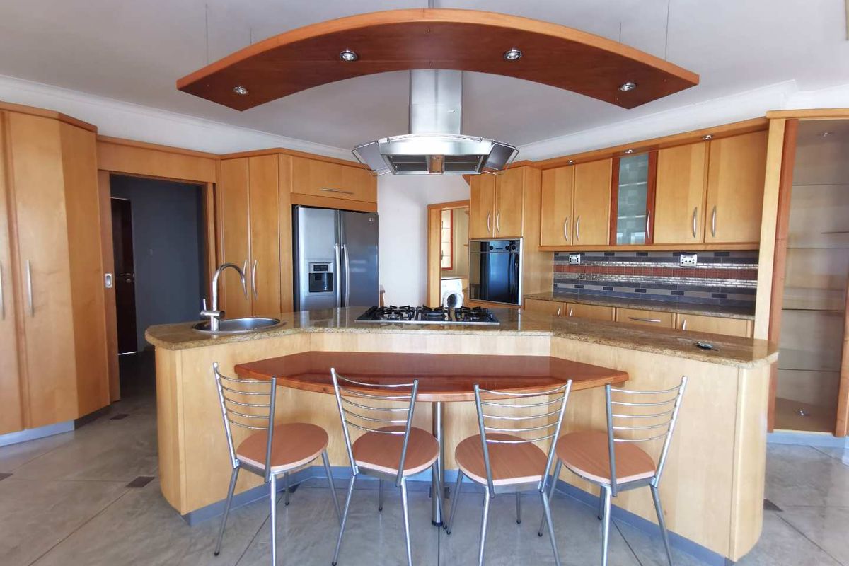 Spacious kitchen featuring light wood cabinetry, granite countertops, a central island with integrated gas hob, and a suspended extractor fan canopy.